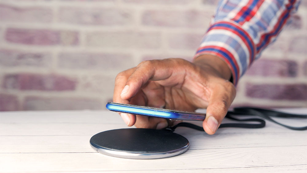 Mão posicionando smartphone sobre base sem fio, ilustrando a tecnologia de carregamento por indução de forma prática e moderna.